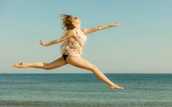 Kvinna som bär klänning spelar, hoppning nära havet — Stockfoto