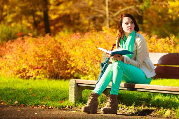 Nainen lukemassa kirjaa istuu penkillä puistossa — kuvapankkivalokuva
