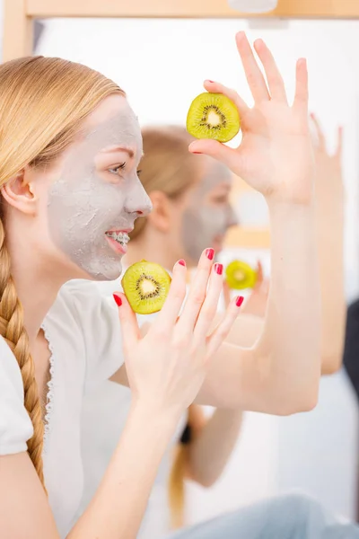 Gelukkig jonge vrouw met gezicht masker bedrijf kiwi — Stockfoto
