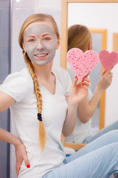 Mujer con máscara facial gris sosteniendo esponja de corazón — Foto de Stock