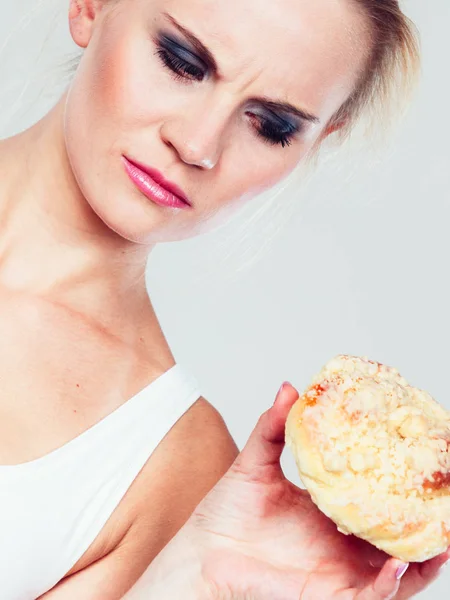 Undecided woman holds cake sweet bun in hand — Stock Photo, Image