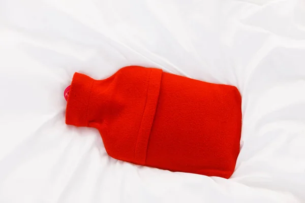Botella de agua caliente roja caliente sobre ropa de cama blanca — Foto de Stock