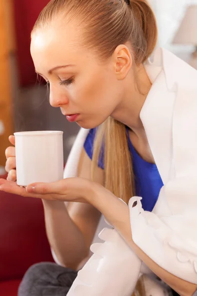 Woman lying on sofa under blanket drinking tea — Stock Photo, Image