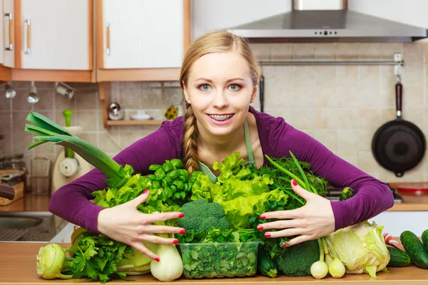 Femme souriante dans la cuisine avec des légumes verts — Photo