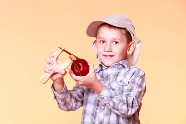 Young boy use sling shot shoot apple. — Stock Photo, Image