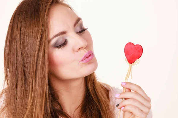Флиртующая женщина держит красное деревянное сердце на палочке — стоковое фото