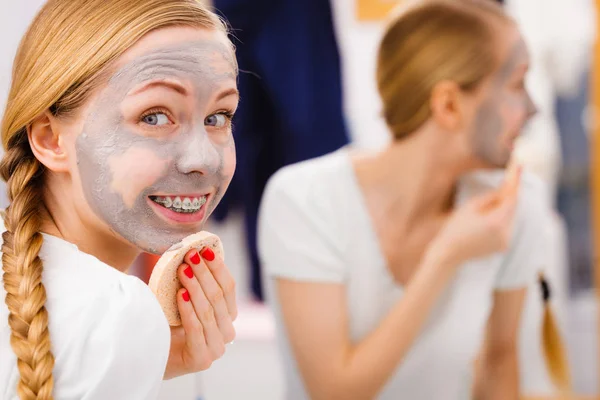 Mulher removendo máscara facial de lama com esponja — Fotografia de Stock