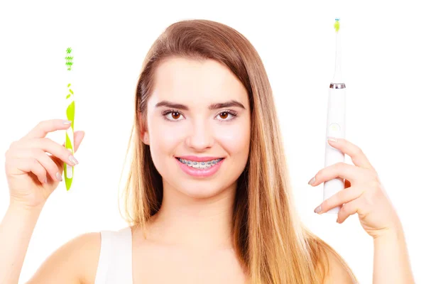 Frau mit Zahnspange hält elektrische und traditionelle Zahnbürste — Stockfoto