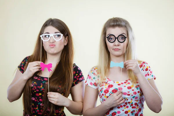 Deux femmes sérieuses tenant des accessoires de carnaval sur bâton — Photo