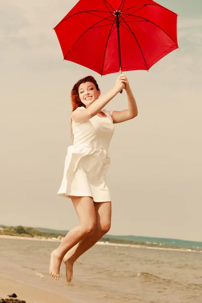 Redhead woman walking on beach jumping with umbrella — Stock Photo, Image