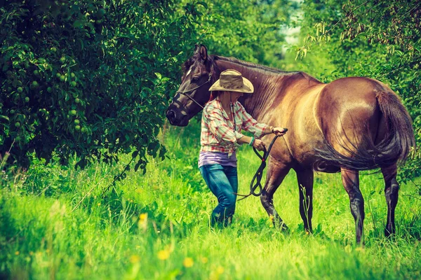 Western woman walking on green meadow with horse — Stock Photo, Image