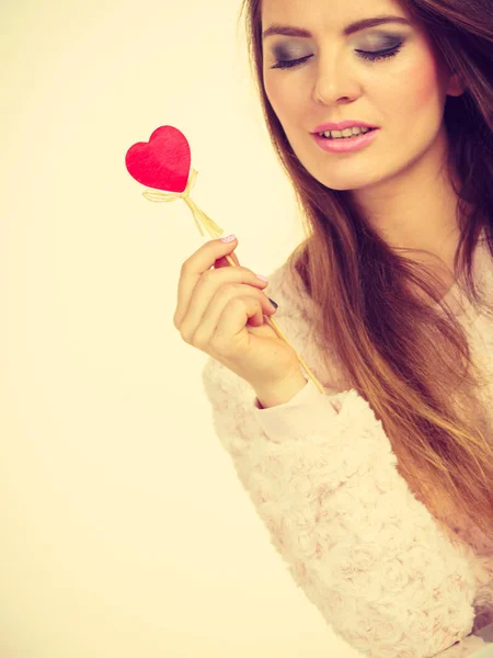 Флиртующая женщина держит красное деревянное сердце на палочке — стоковое фото