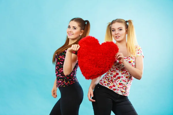 Feliz dos mujeres sosteniendo almohada en forma de corazón —  Fotos de Stock