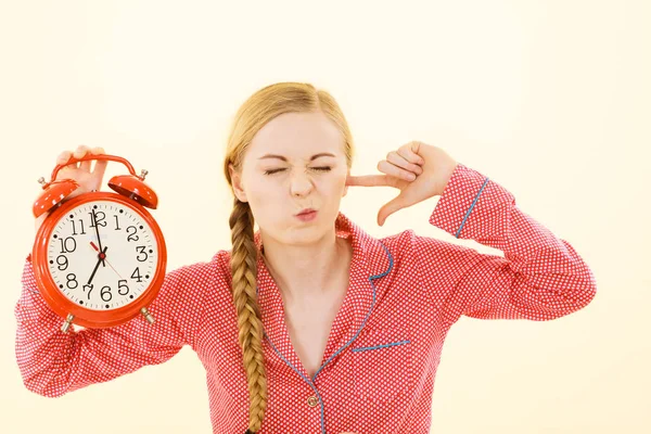 Sömnig kvinna klädd i pyjamas håller klockan — Stockfoto