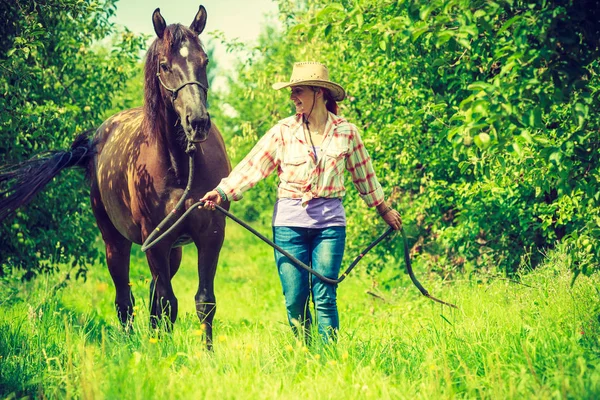 Westerse vrouw lopen op groene weide met paard — Stockfoto