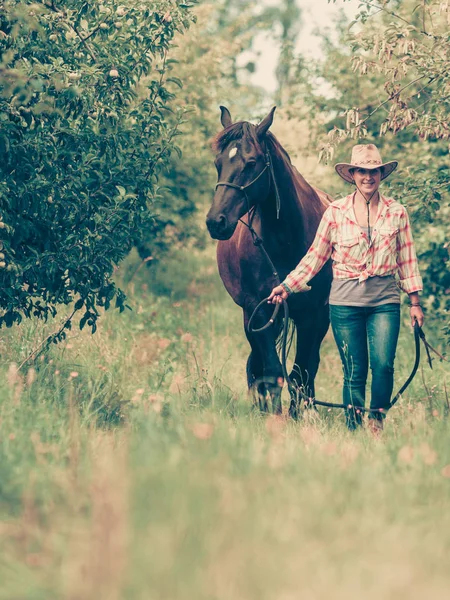 Mulher ocidental andando no prado verde com cavalo — Fotografia de Stock