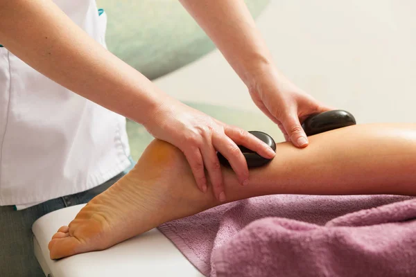 Masseuse doing legs massage with hot stones — Stock Photo, Image