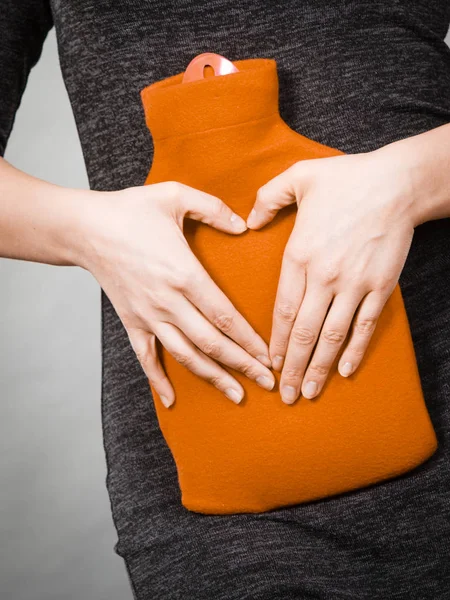 Girl holds hot water bottle on belly making heart shape by hands — Stock Photo, Image