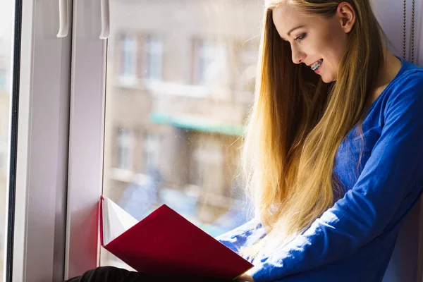 Evde kitap okuma pencere pervazına üzerinde oturan kadın — Stok fotoğraf