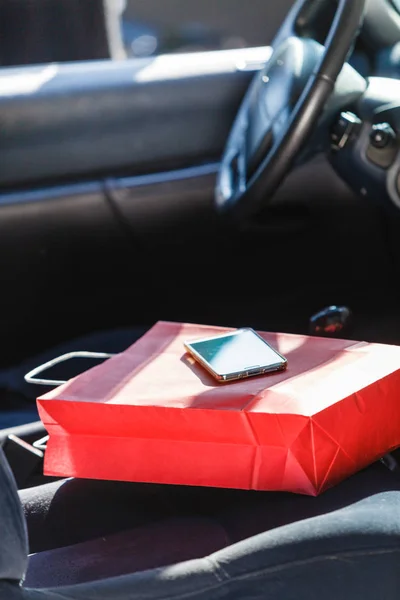 Bolsa de compras y teléfono inteligente tumbado en el asiento del coche — Foto de Stock