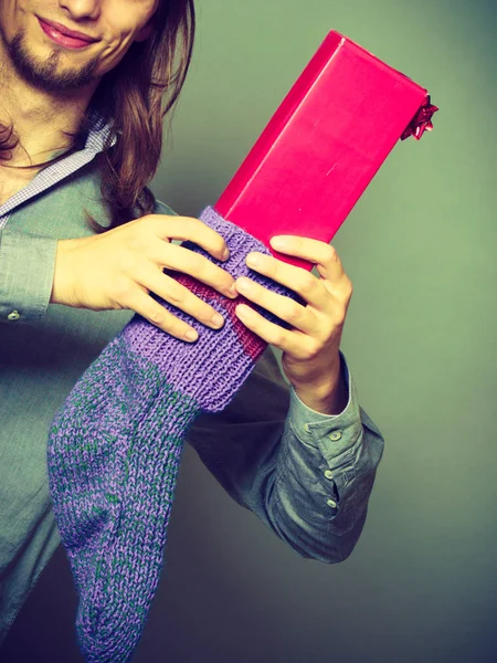 Guy putting wrapped gift in knitted christmas sock — Stock Photo, Image