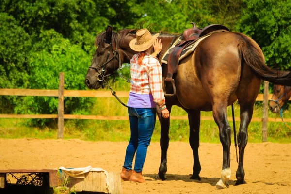 Cowgirl getting horse ready for ride on countryside — Stock Photo, Image