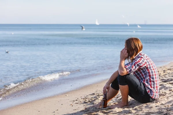 屋外のビーチに座っているワインのボトルと、落ち込んで人 — ストック写真