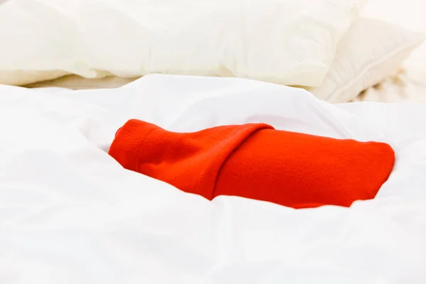 Warm red hot water bottle on white bedding — Stock Photo, Image