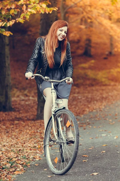 Menina de cabelos vermelhos andando de bicicleta no parque outonal — Fotografia de Stock