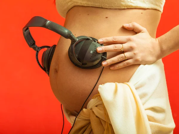 戴着耳机在孕妇的肚子上的女人 — 图库照片