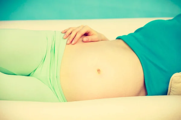 Mujer embarazada acostada en el sofá tocando su vientre — Foto de Stock