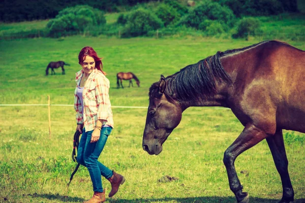 Westerse vrouw lopen op groene weide met paard — Stockfoto