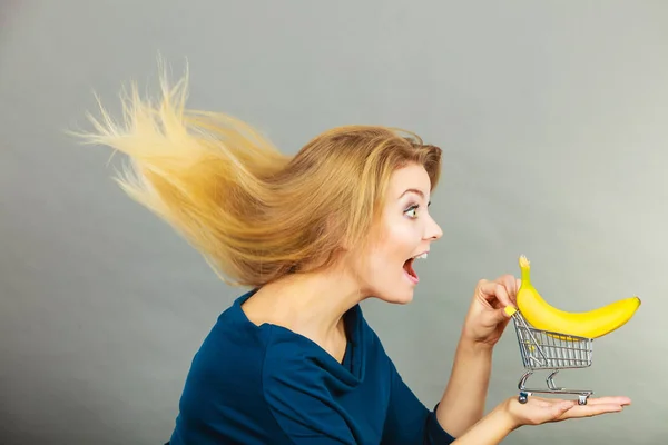 Mulher segurando carrinho de compras com banana dentro — Fotografia de Stock