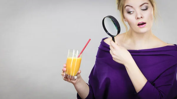 Woman holding magnifying glass investigating juice — Stock Photo, Image