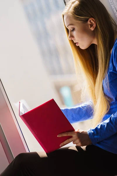 Mujer sentada en el alféizar de la ventana leyendo libro en casa —  Fotos de Stock