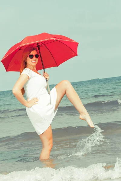 Рыжая женщина ходит по пляжу с зонтиком в руках — стоковое фото