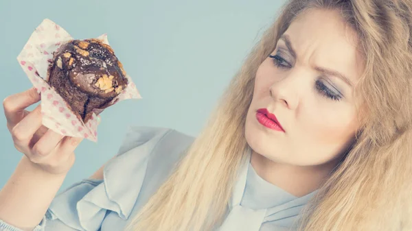 Скептична жінка тримає шоколадний кекс — стокове фото