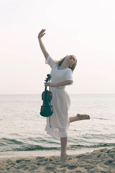 Woman on beach near sea holding violin — Stock Photo, Image