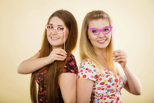 Dos mujeres felices sosteniendo anteojos falsos en palo — Foto de Stock