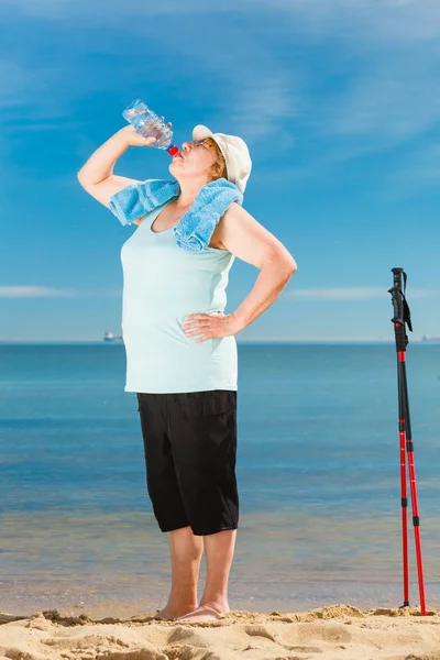 Senior woman practicing nordic walking on beach — Stock Photo, Image