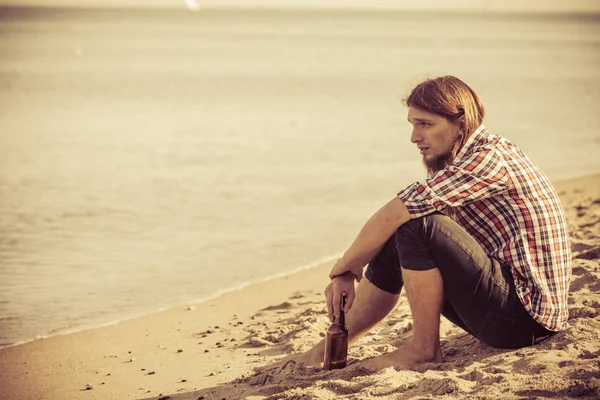 Man depressed with wine bottle sitting on beach outdoor — Stock Photo, Image