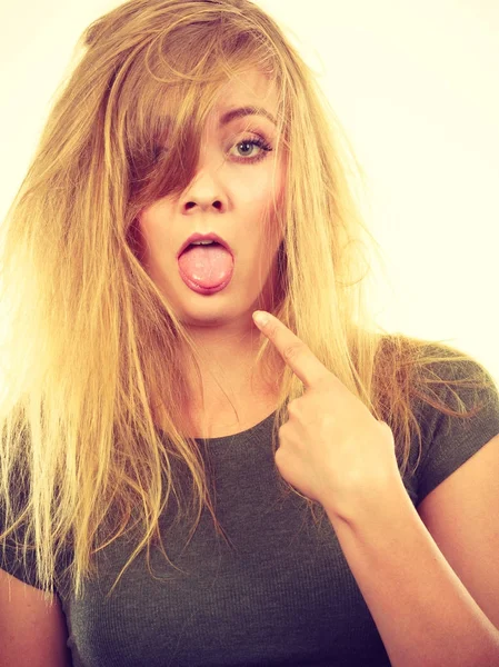 Sorgliga blond kvinna med stökigt hår pekar tungan — Stockfoto