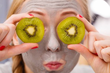 Happy young woman having face mask holding kiwi clipart
