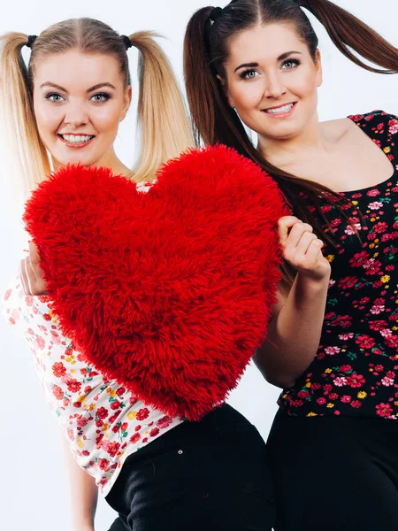 Feliz dos mujeres sosteniendo almohada en forma de corazón —  Fotos de Stock