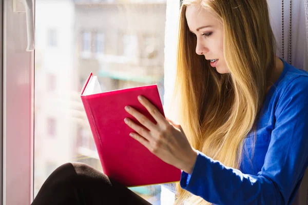 Woman sitting on window sill reading book at home — Stock Photo, Image