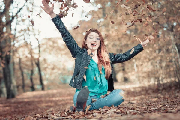 Ginger girl spelar med blad i park. — Stockfoto