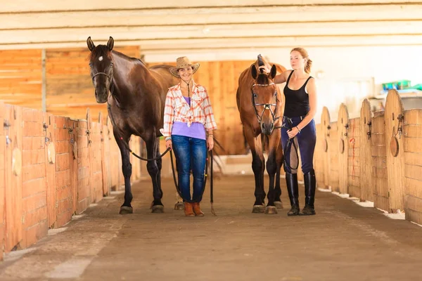 Cowgirl und Jockey gehen mit Pferden im Stall — Stockfoto