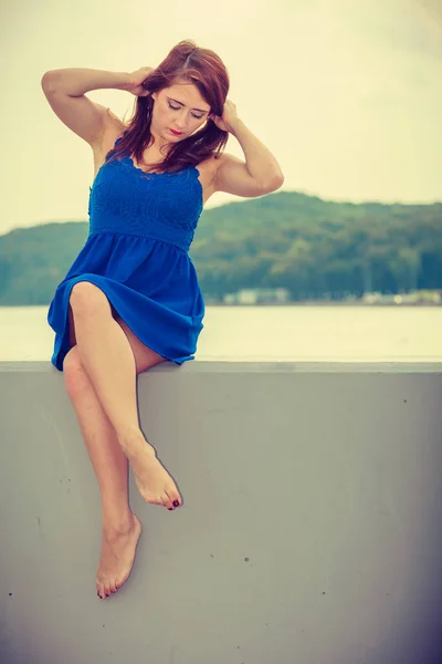 Melancholic woman in short dress sitting on jetty — Stock Photo, Image