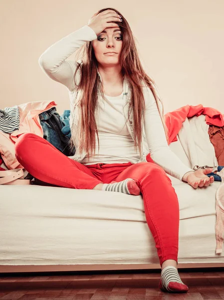 Mulher confusa sente-se no sofá cheio de roupas . — Fotografia de Stock