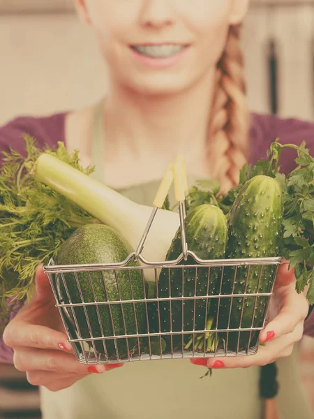 Kvinna i köket med grönsaker håller varukorg — Stockfoto